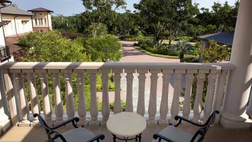 Un balcón con una mesa y dos sillas, con vista a un jardín ajardinado con árboles y un sendero.