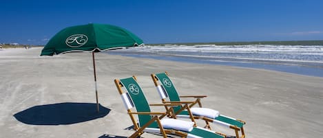 Two beach chairs with green towels and a matching umbrella on a sandy beach.