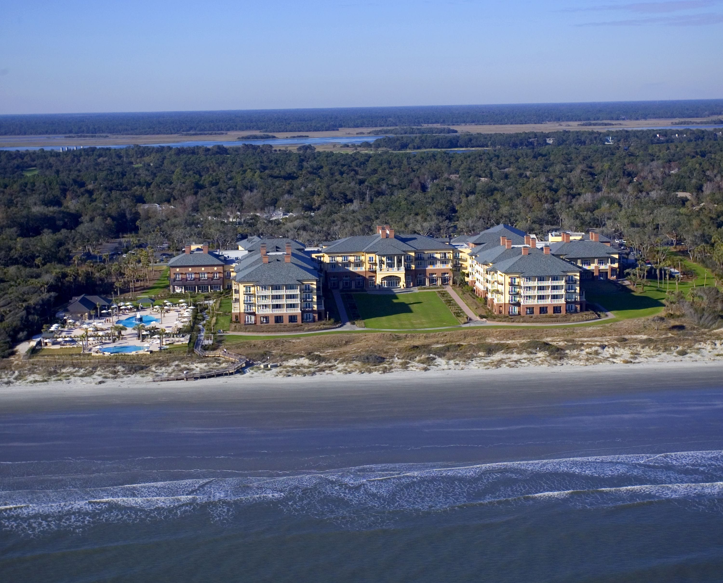Un resort costero con varias edificaciones, una piscina y vista a la playa.