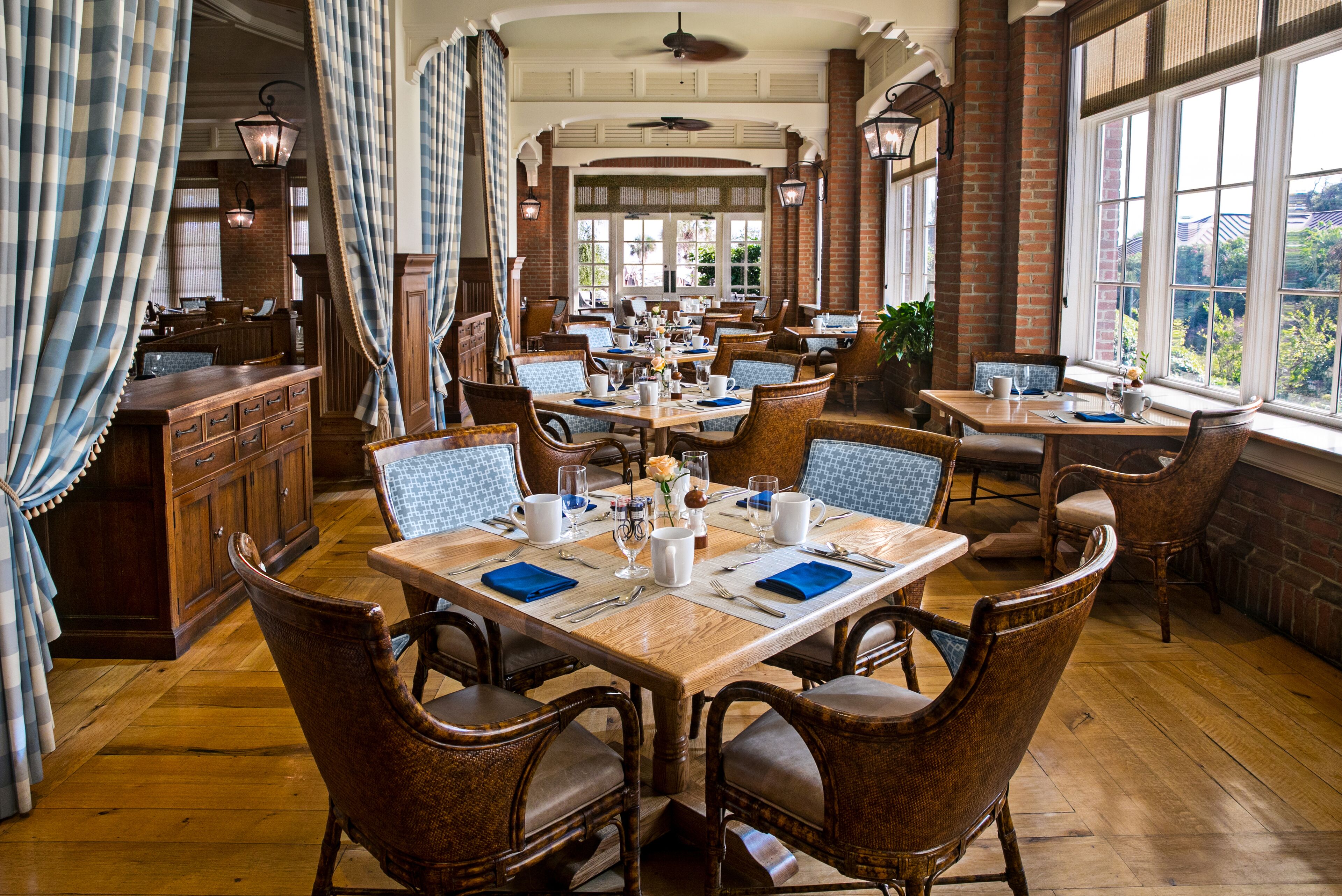 A restaurant with wooden tables and chairs, brick walls, and large windows offering a view.