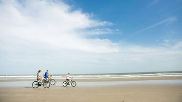 Une scène de plage où l’on voit trois personnes faire du vélo.