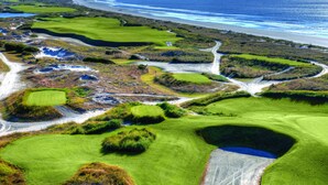 Um campo de golfe com vários greens, bunkers e vista para o litoral.
