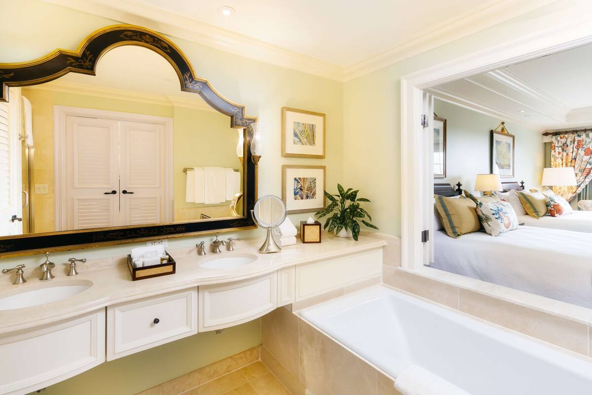 A bathroom with a large mirror, two sinks, a bathtub, and a toilet.