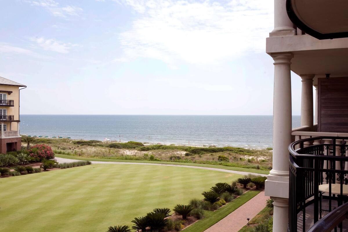 A view of a golf course with a building in the foreground and the ocean in the background.