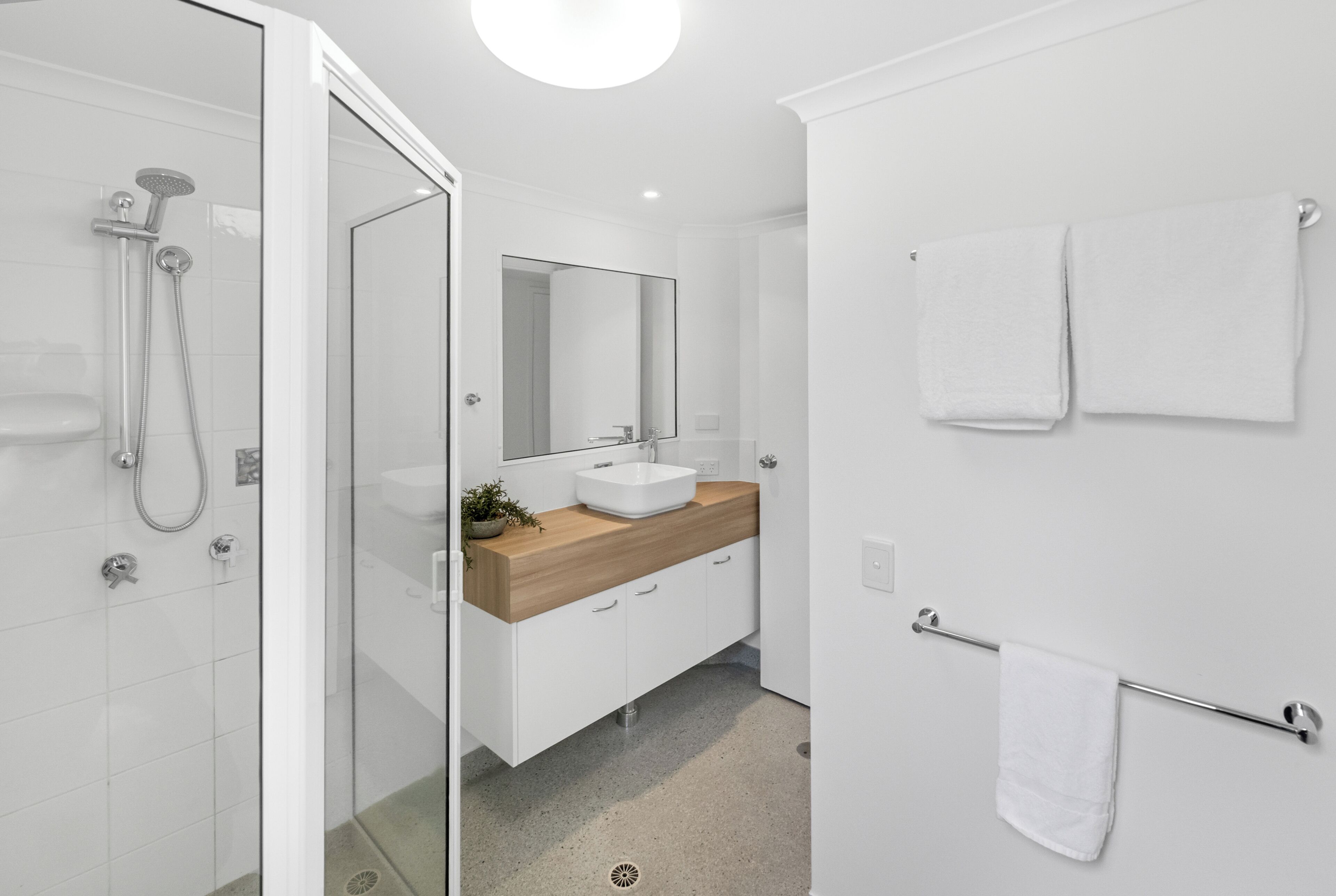 Un baño moderno con cabina de ducha de vidrio, tocador de madera, espejo grande y barra para toallas.