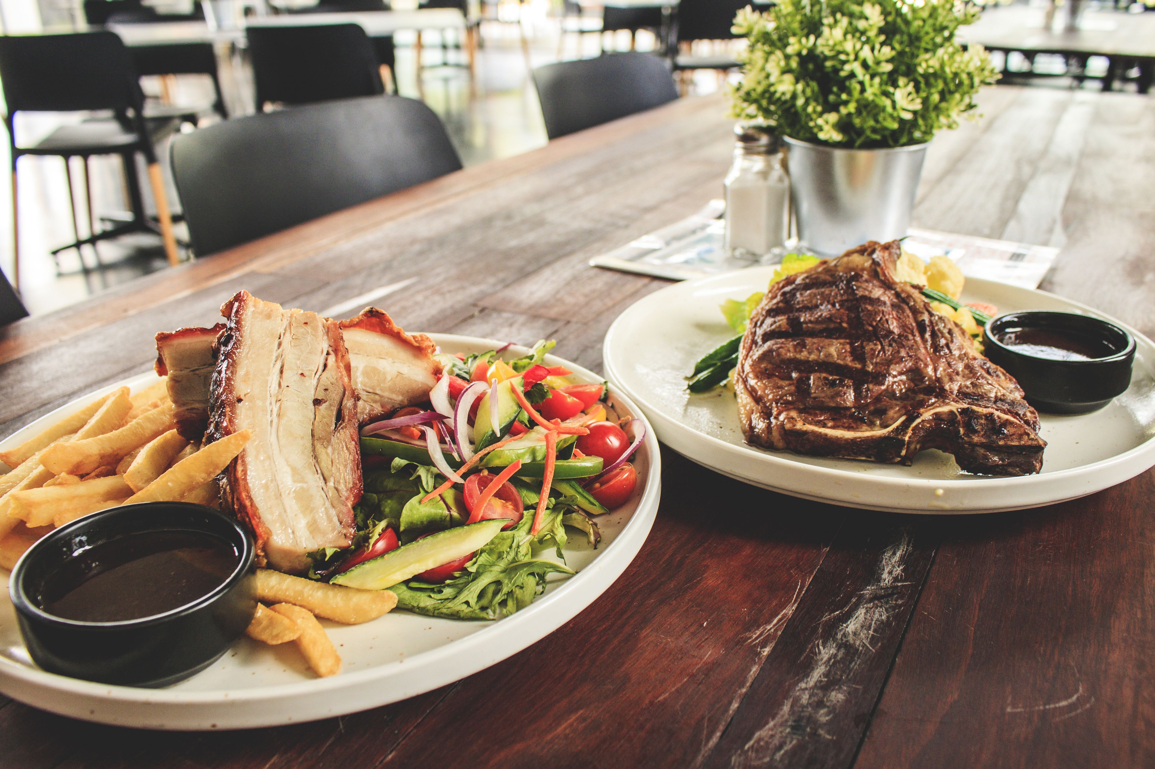 Una mesa de madera con dos platos de comida, uno con ensalada y papas fritas y el otro con un bistec y un acompañamiento.