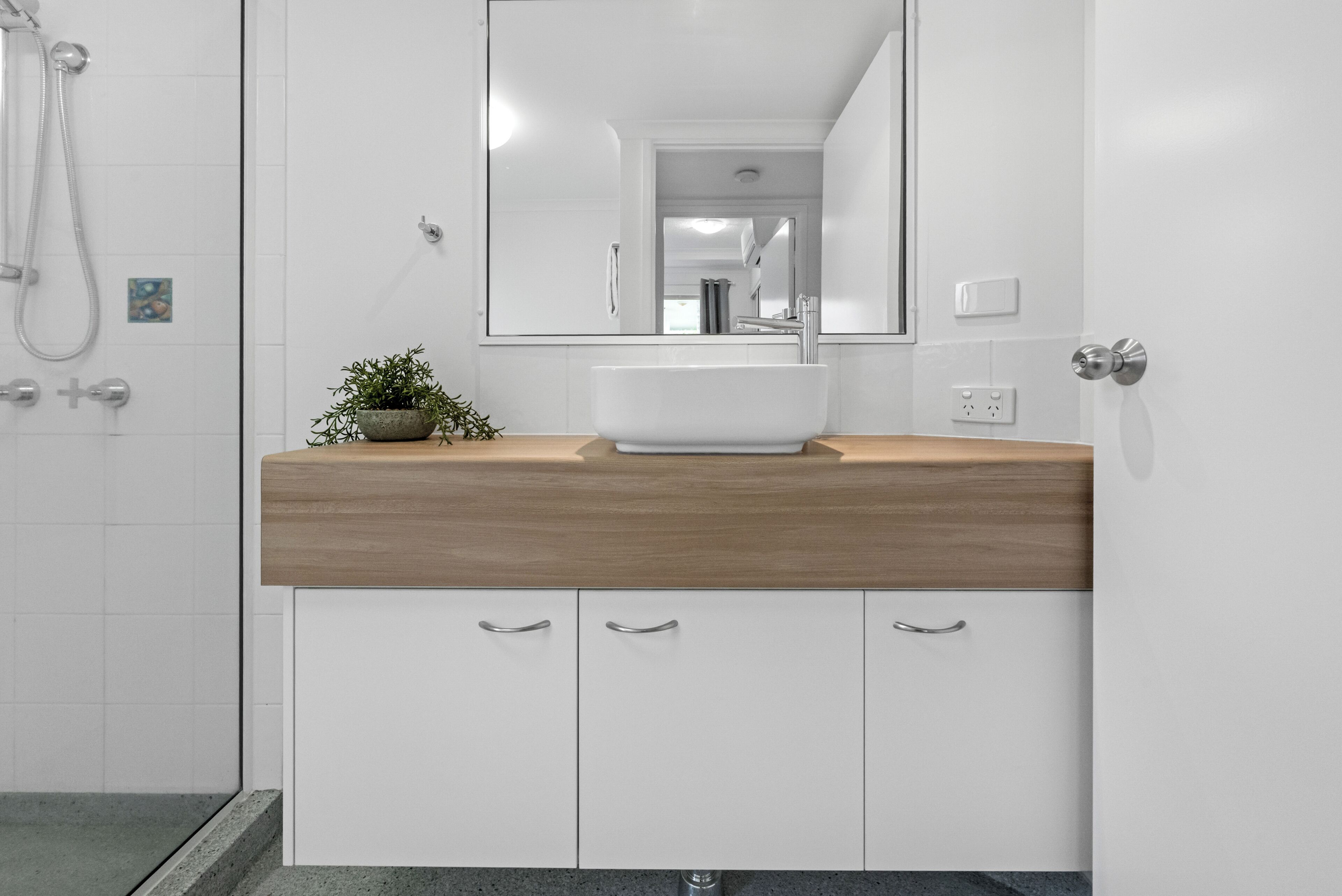 A bathroom with a white sink, wooden countertop, and a mirror.