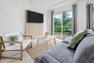 Una sala de estar moderna con un sofá, una silla de madera, una mesita y un televisor de pantalla plana montado en la pared.
