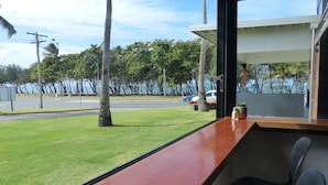 A view from a room with a wooden desk and a chair, overlooking a street with parked cars and a line of trees. - Mackay Seabreeze Apartments (Slade Point)