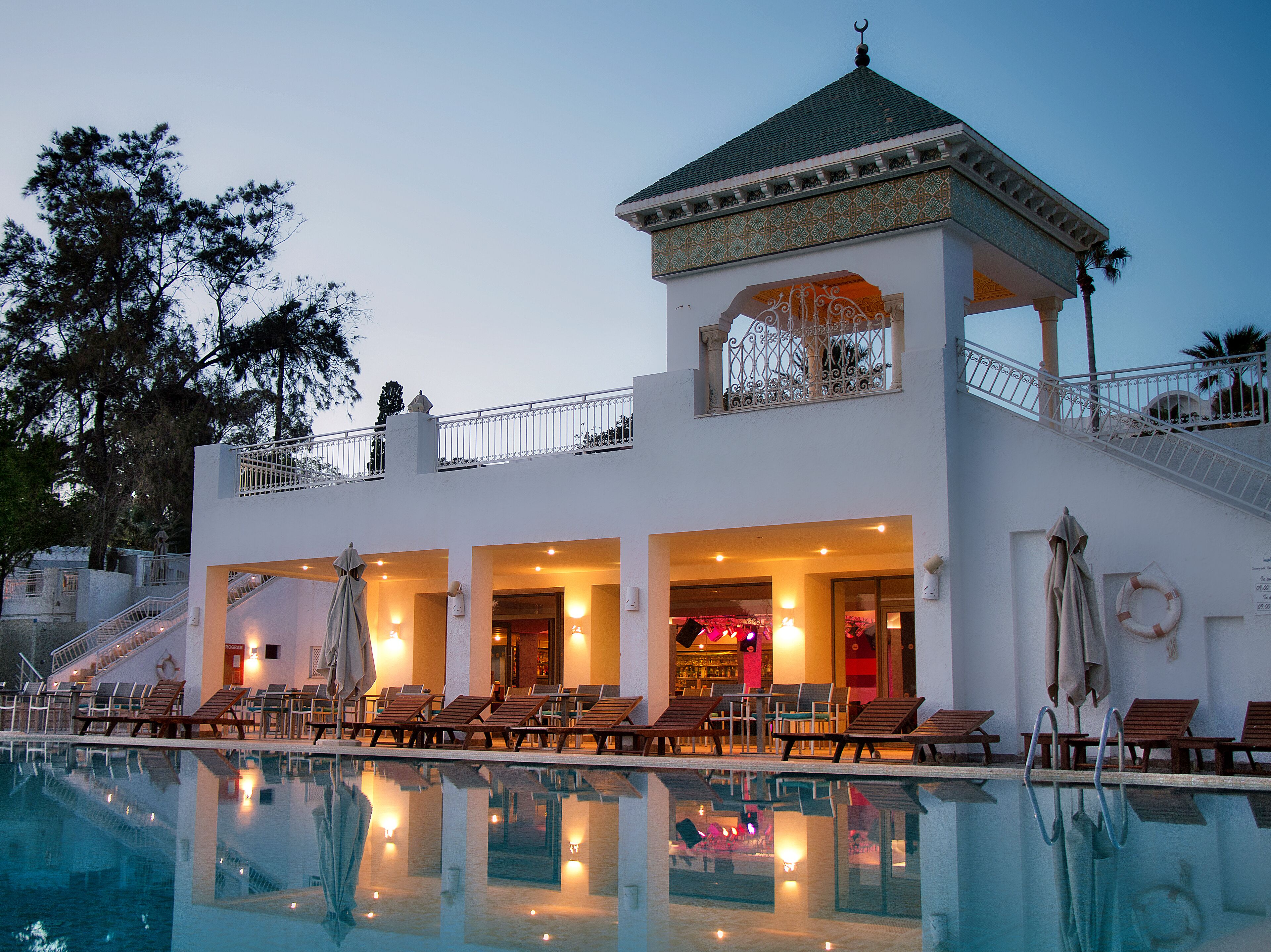 A hotel with a pool, lounge chairs, and a covered area with a decorative ceiling.