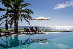 Una piscina infinita con vistas despejadas al océano, palmeras y sillones de descanso.