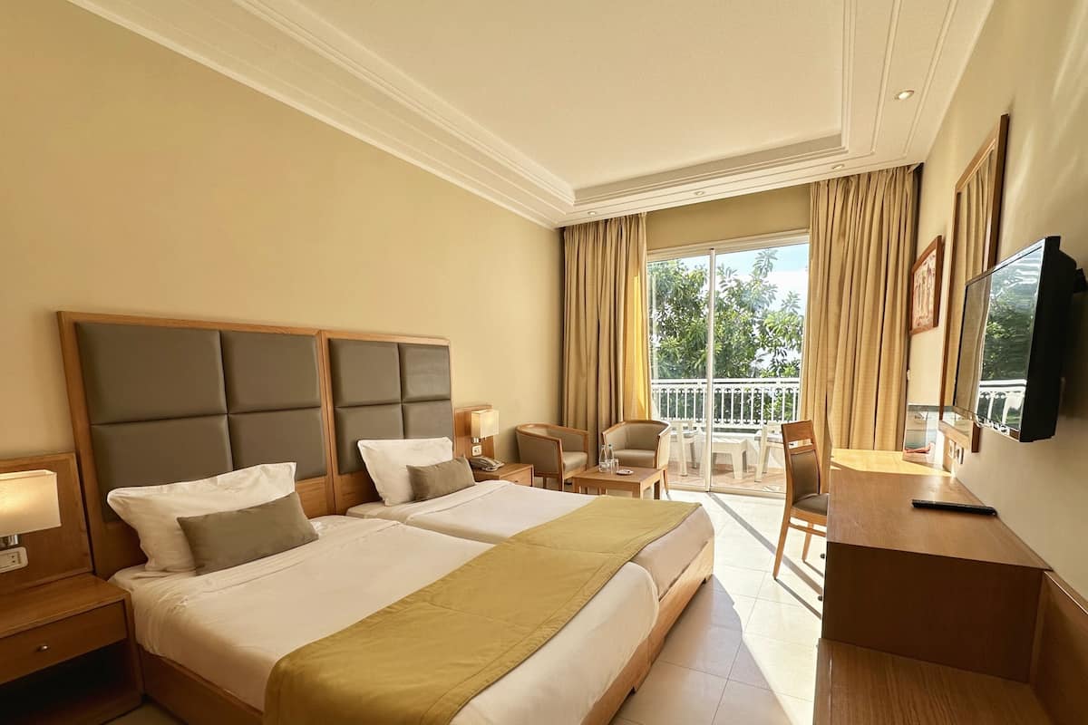 Habitación de hotel con dos camas, un balcón, un escritorio y un televisor.