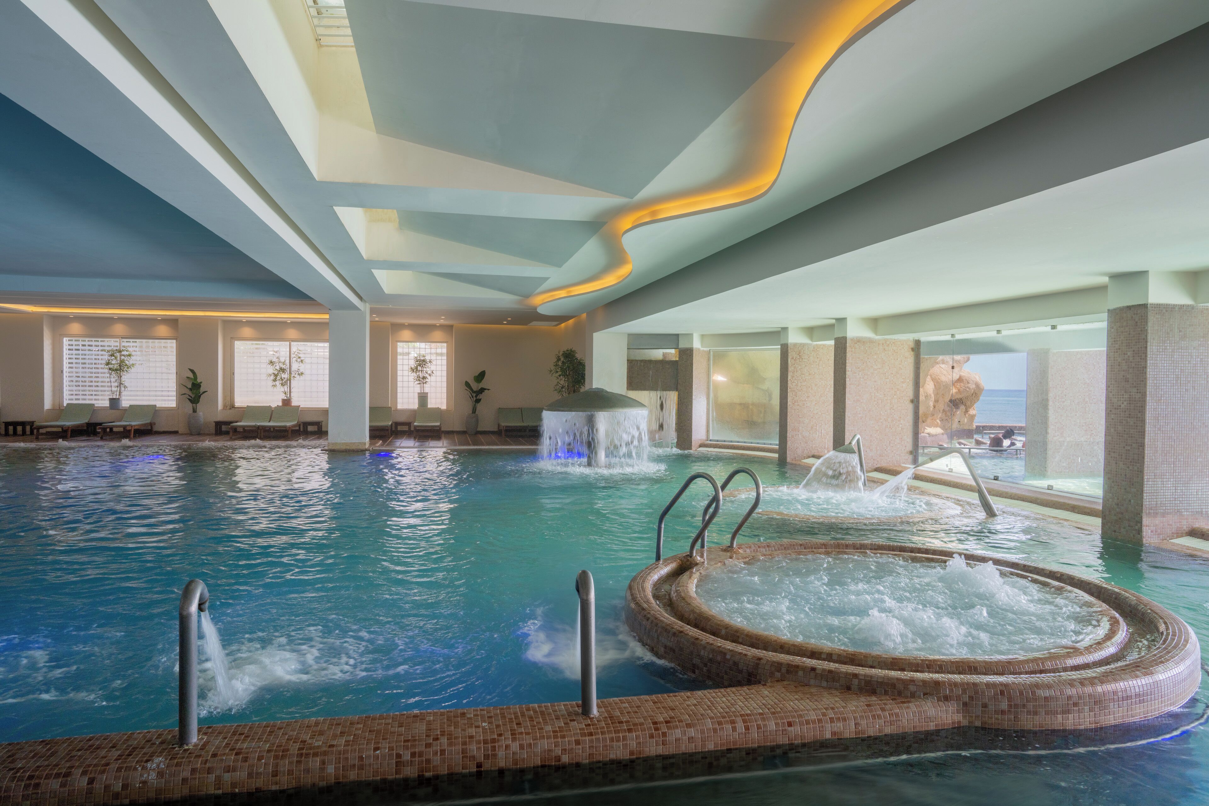 Une piscine intérieure dotée d’un jacuzzi, d’une eau cristalline et d’une cascade décorative.