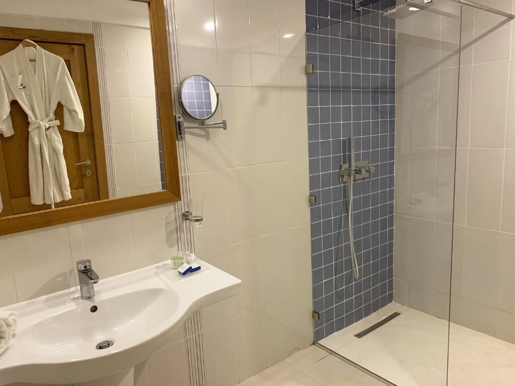 A bathroom with a white sink, a mirror, and a glass-enclosed shower with blue tiles.