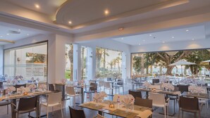Um restaurante espaçoso com várias mesas e cadeiras, grandes janelas que oferecem vista para o exterior e um design de interiores moderno.
