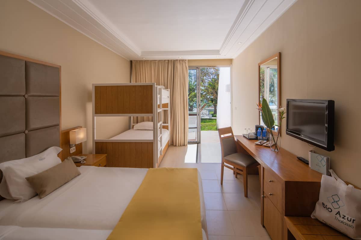 Una habitación de hotel con cama, escritorio, televisor y balcón con cortinas.