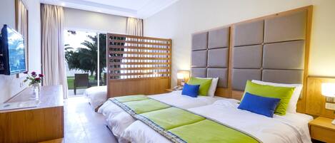Habitación de hotel con una cama grande, una mesita de noche de madera, un televisor y vistas al exterior.