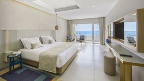A modern hotel room with a large bed, a desk, a chair, and a balcony with a view of the sea. - Royal Azur Thalassa (Hammamet)