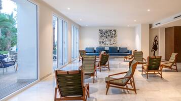 Un hall d’entrée spacieux, avec un canapé bleu moderne, plusieurs chaises en bois et un grand tableau abstrait accroché au mur.