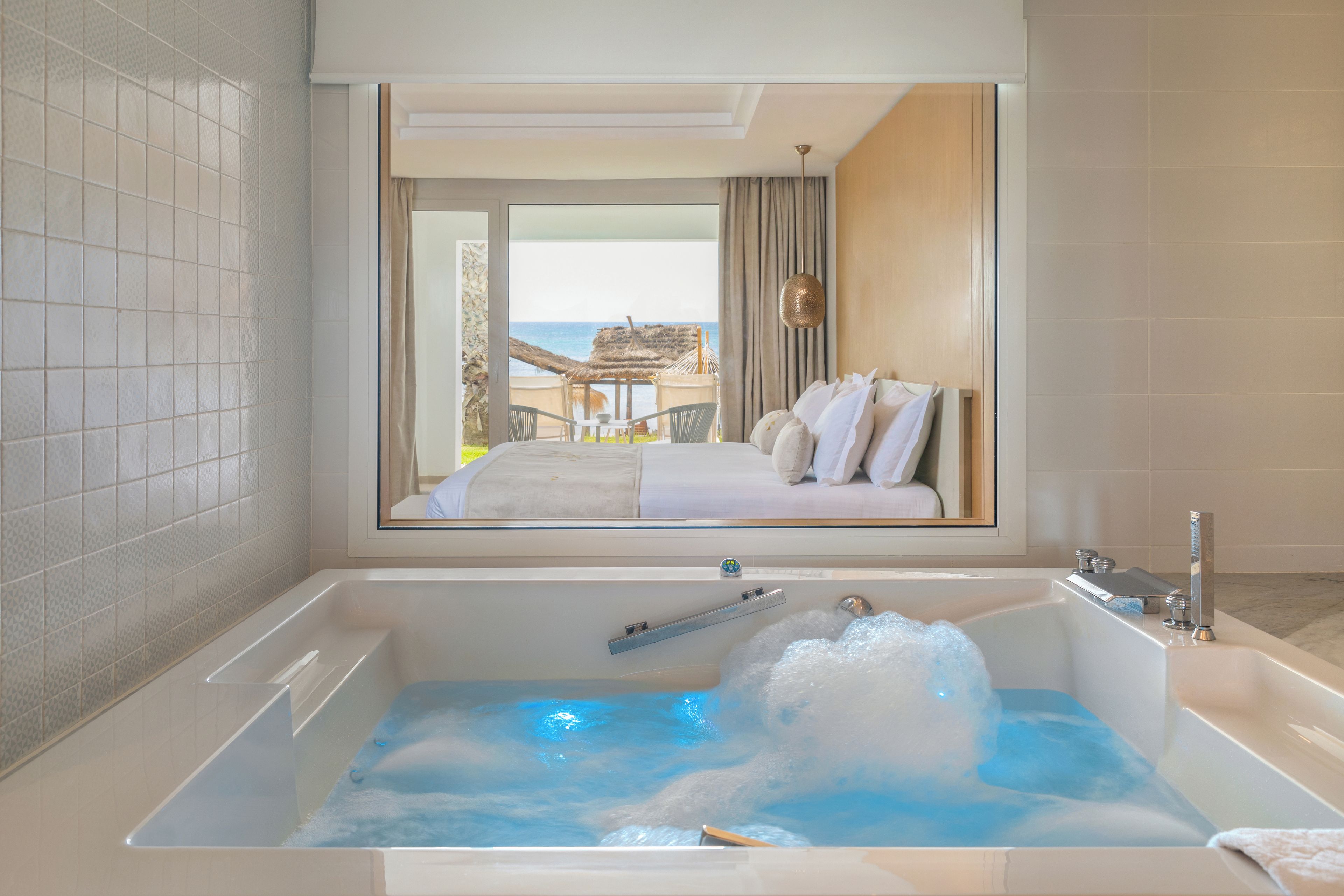 A modern bathroom with a large bathtub, a shower, and a view of a balcony with a table and chairs.