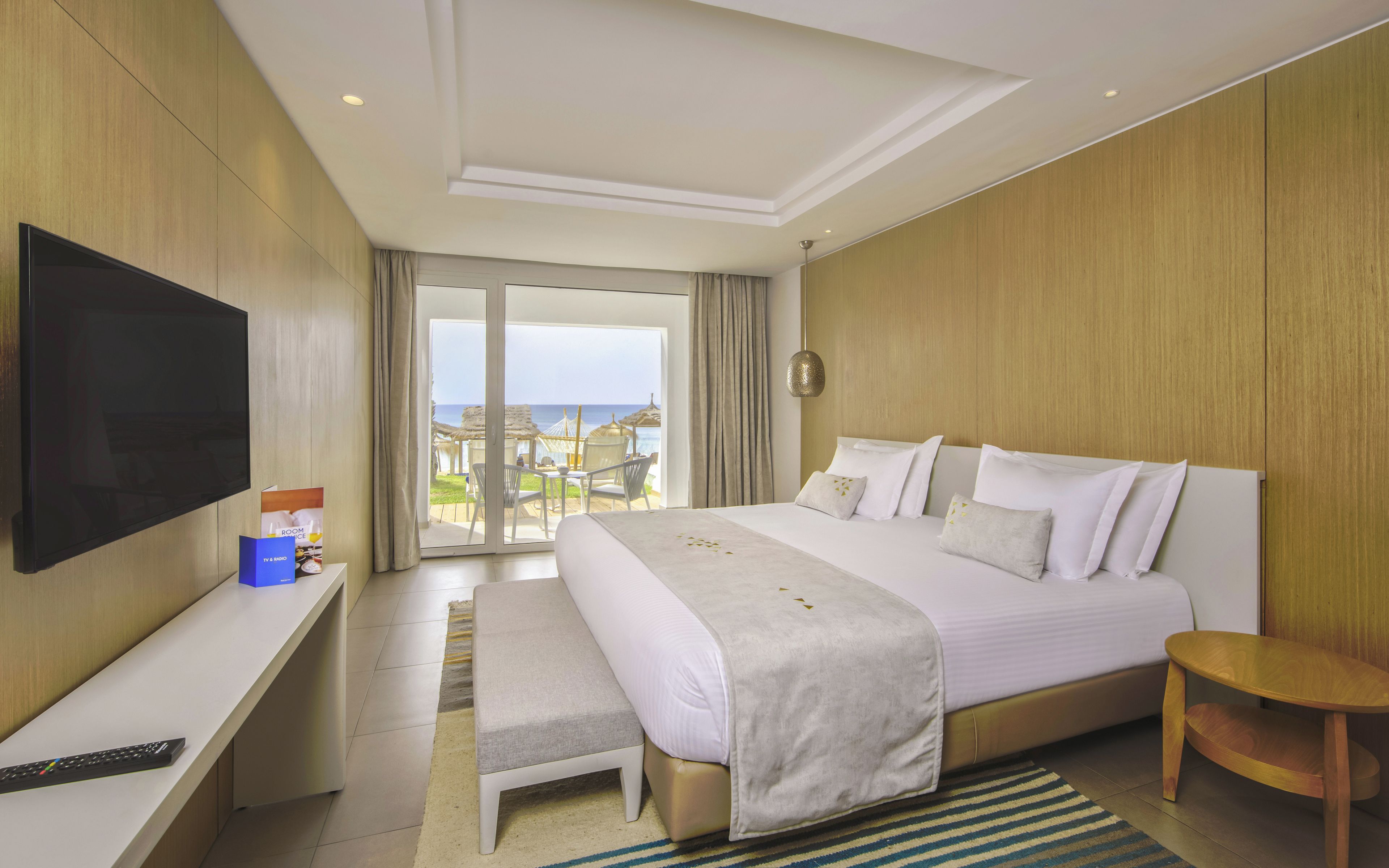 Una habitación de hotel con cama, televisión, escritorio y vista a la playa.