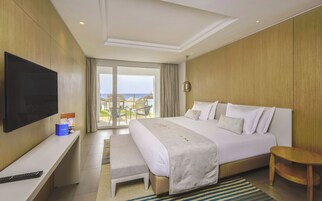 Una habitación de hotel con cama, televisión, escritorio y vista a la playa.