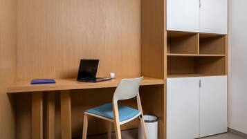 A workspace with a wooden desk, a chair, a laptop, a cup, and a trash bin.