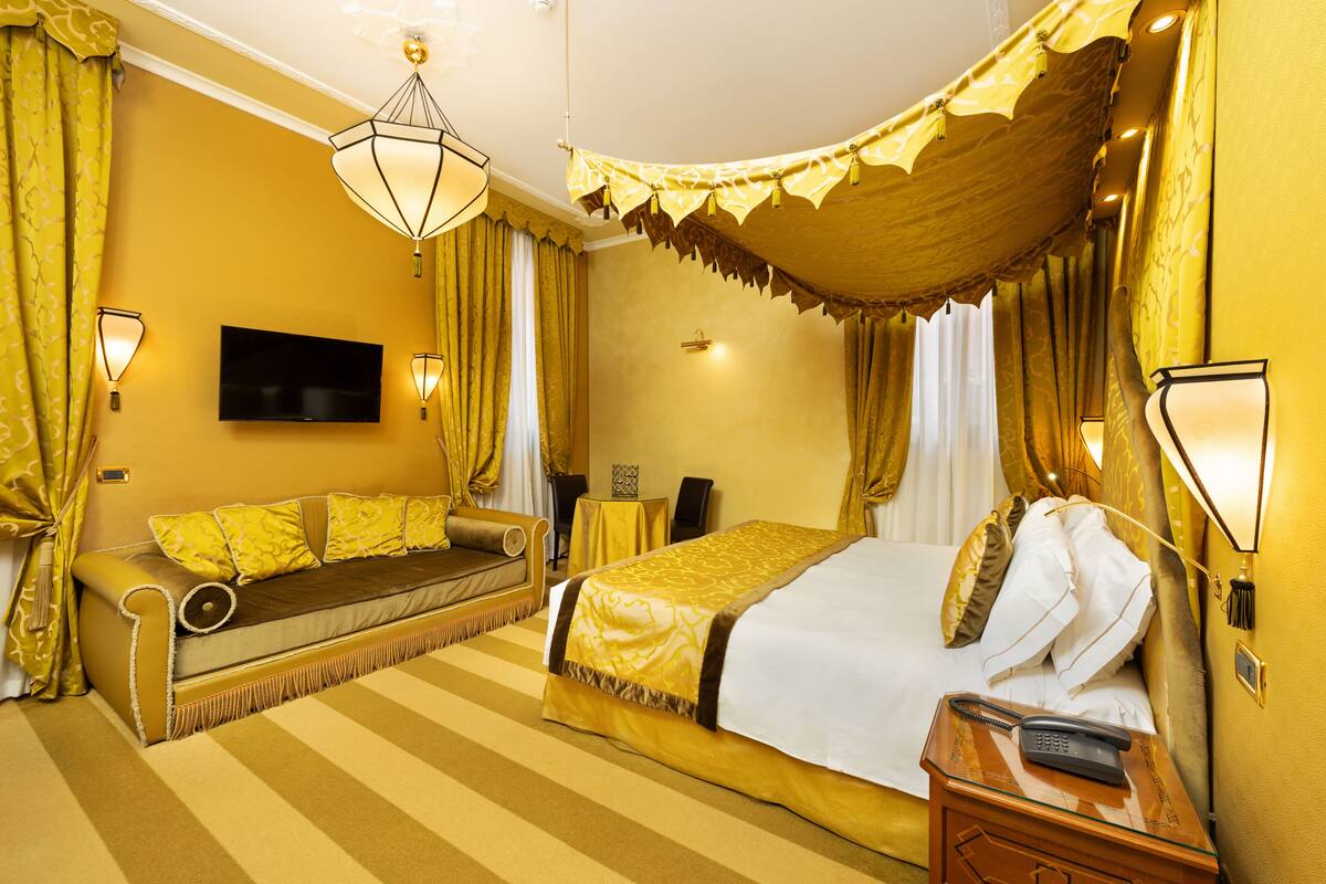 A hotel room with a bed, a sofa, a TV, and a telephone.