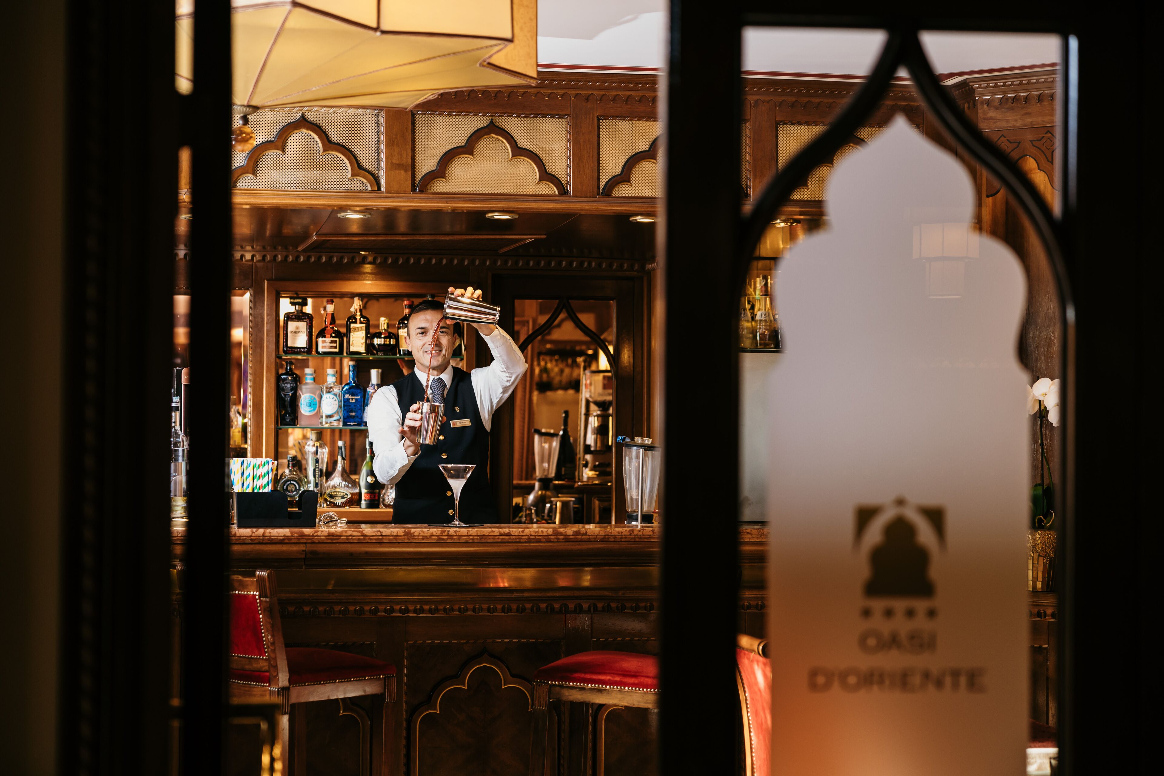 A bar area with a bartender, wooden decor, and a sign reading "OASI DORIENTE".