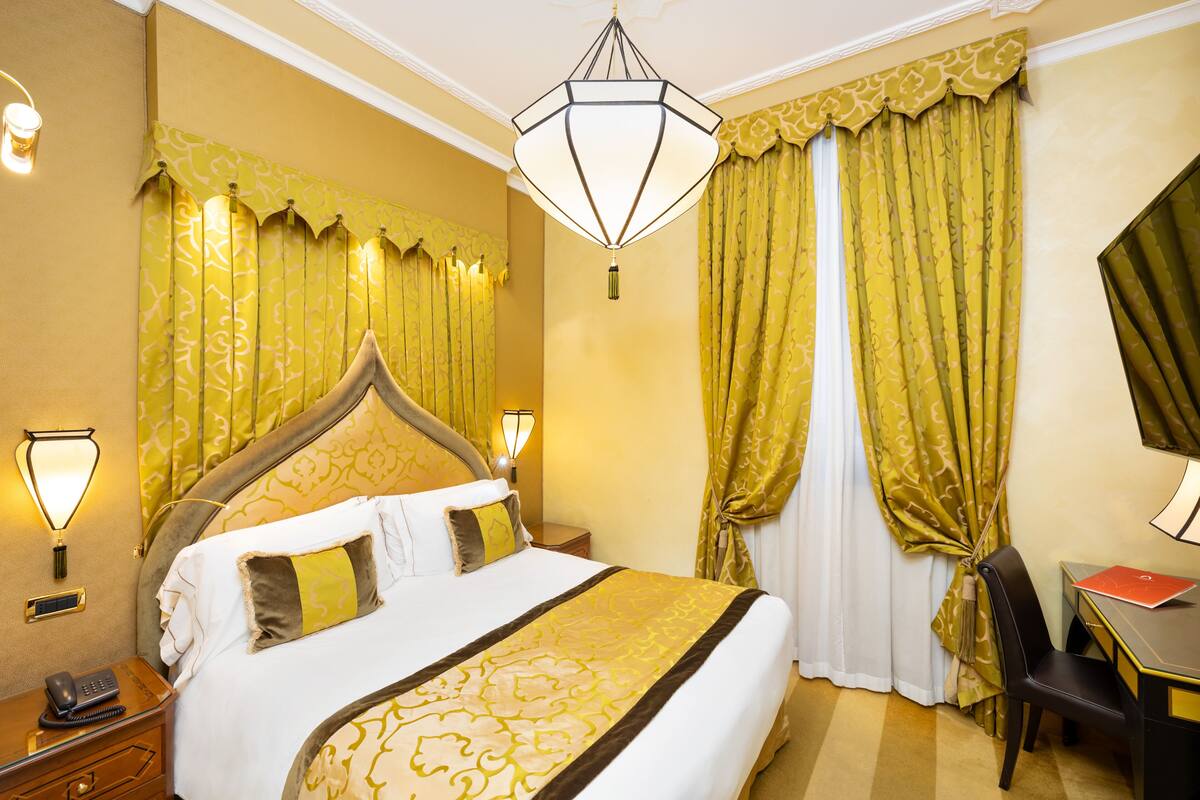 A hotel room with a large bed, a desk with a chair, a telephone, and a lamp.
