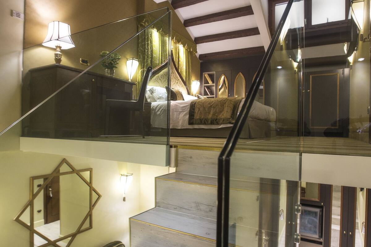 A staircase with glass railings leading to a bedroom with a bed and a nightstand.