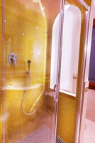 A glass-enclosed shower with yellow mosaic tiles and a visible showerhead.