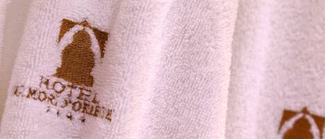 Toalla blanca con texto y logo bordados, que sugiere un entorno hotelero.