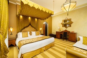 A hotel room with a large bed, a desk, a chair, and a mirror on the wall.