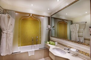 Un baño con una bañera, un lavamanos y un espejo grande. Hay toallas colgadas en un perchero y una cortina de ducha.