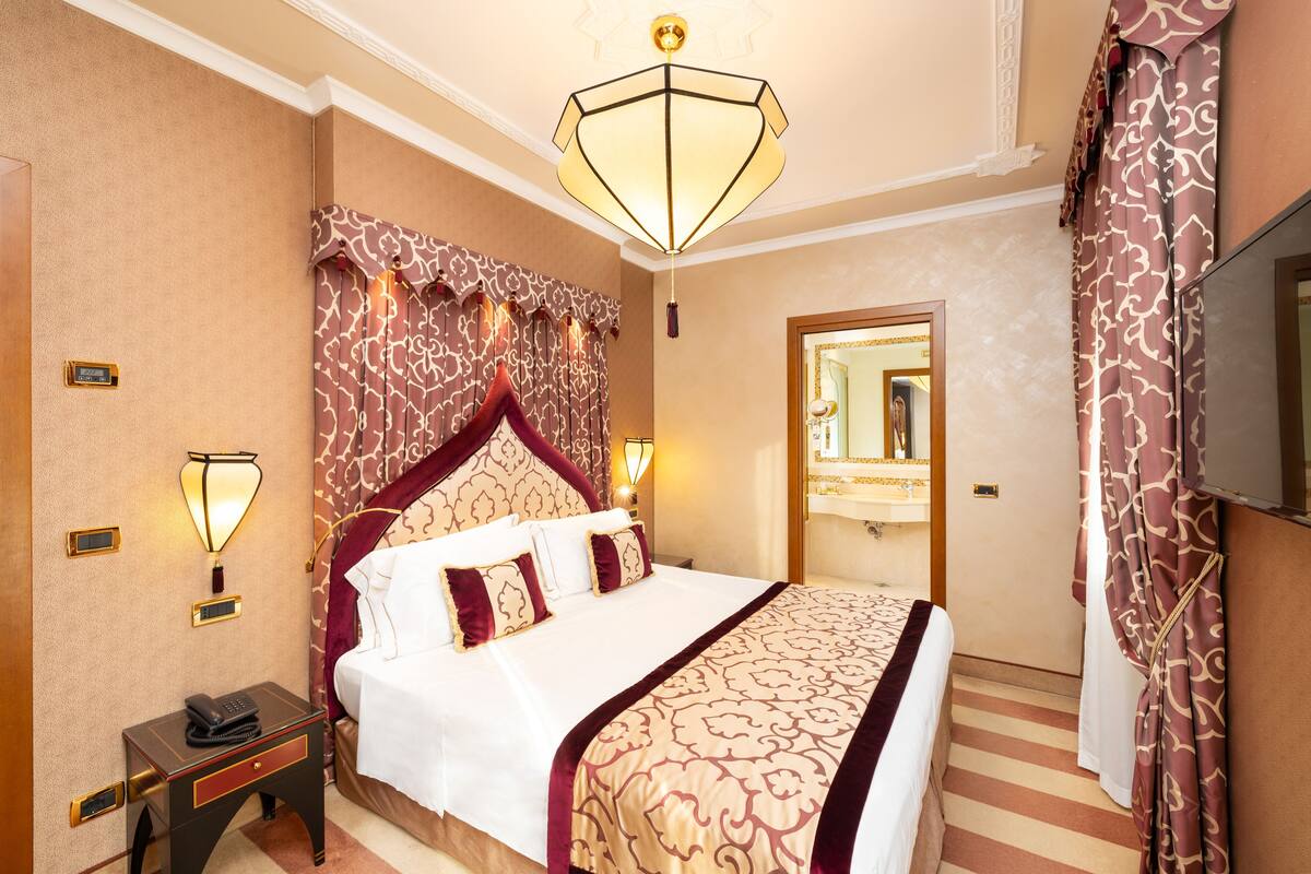 A hotel room with a large bed, a nightstand with a telephone, a wall-mounted lamp, and a mirror.