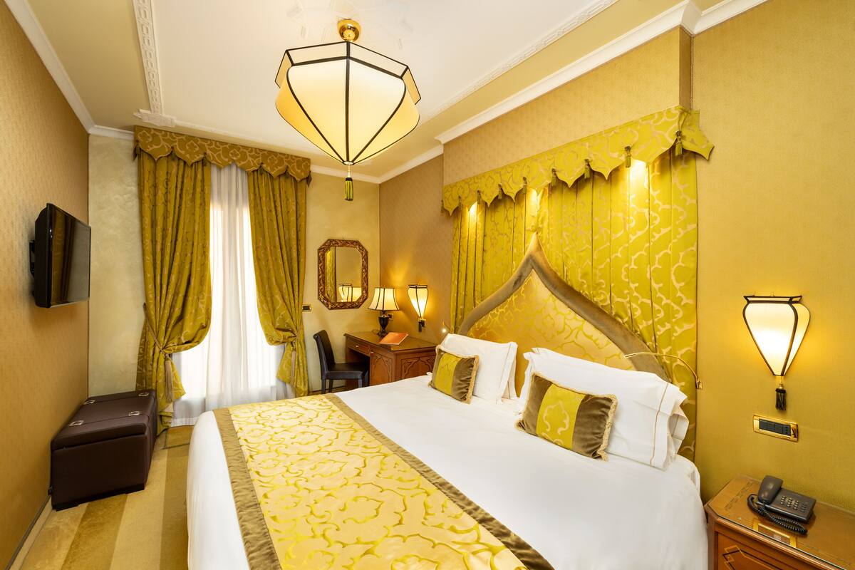A hotel room with a large bed, a desk with a chair, a telephone, and a television.