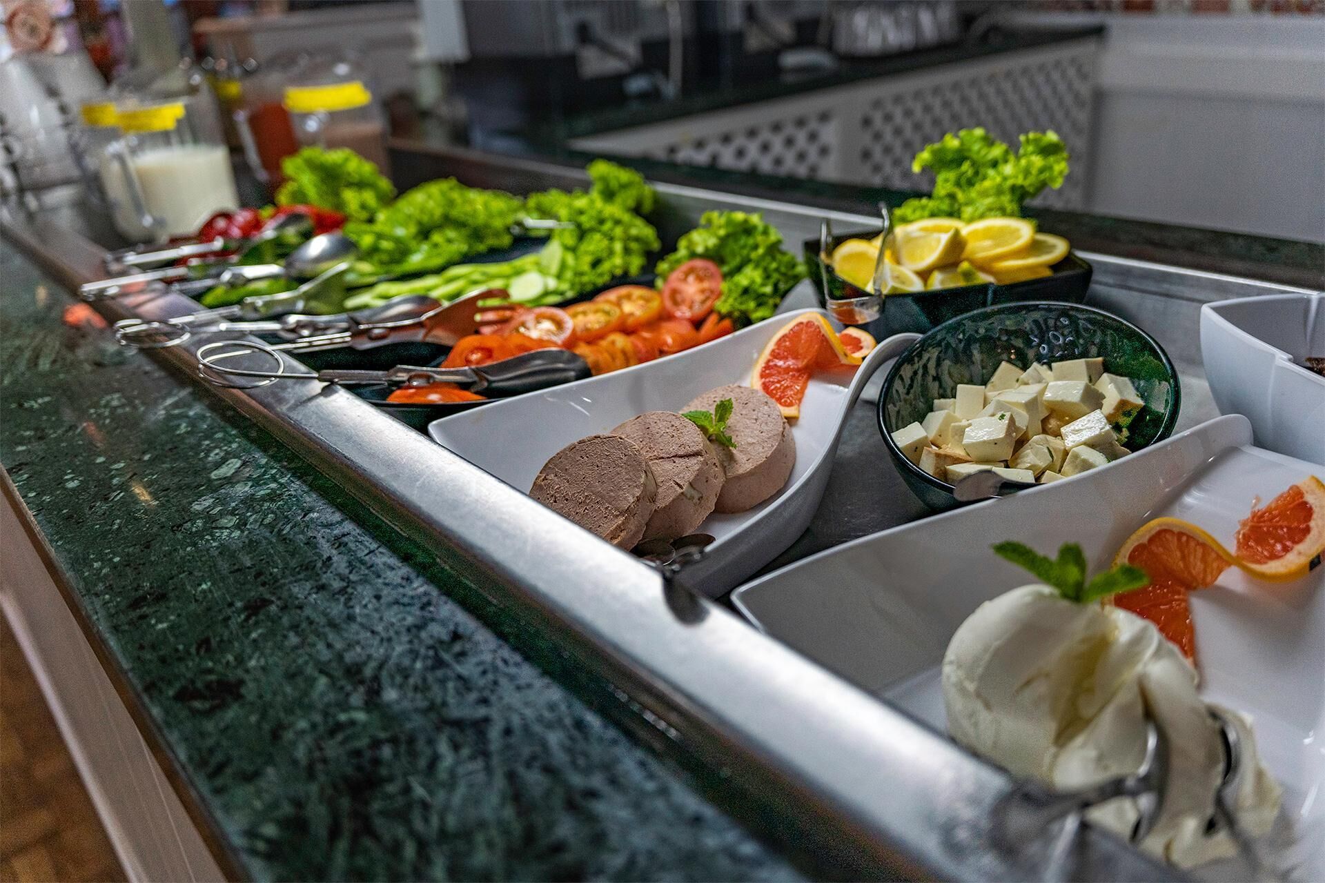 A buffet with various food items including vegetables, fruits, and different types of meat.