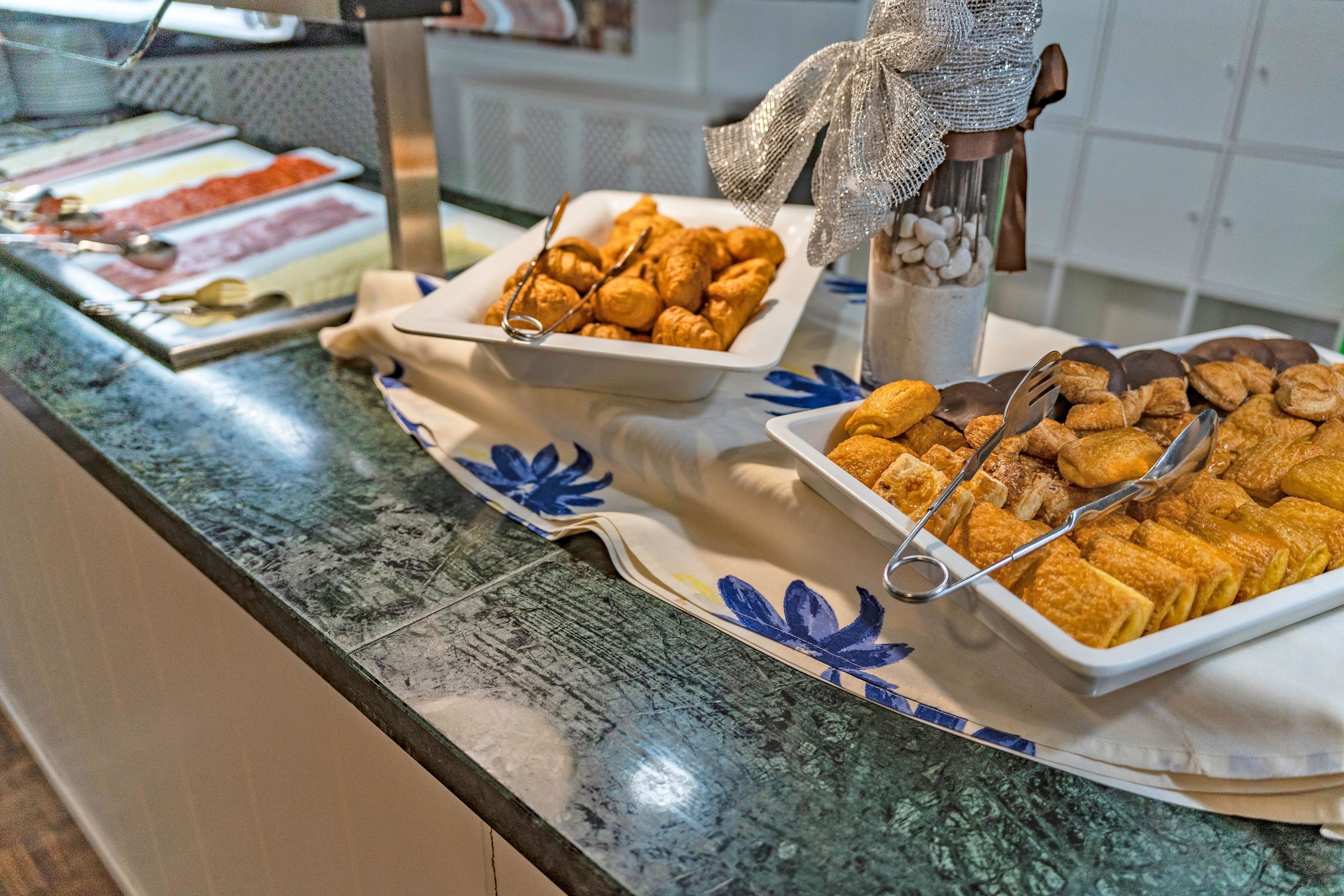 Un bufé con diversas opciones de comida, incluyendo pasteles y carnes, dispuestas sobre un mostrador con un mantel decorativo.