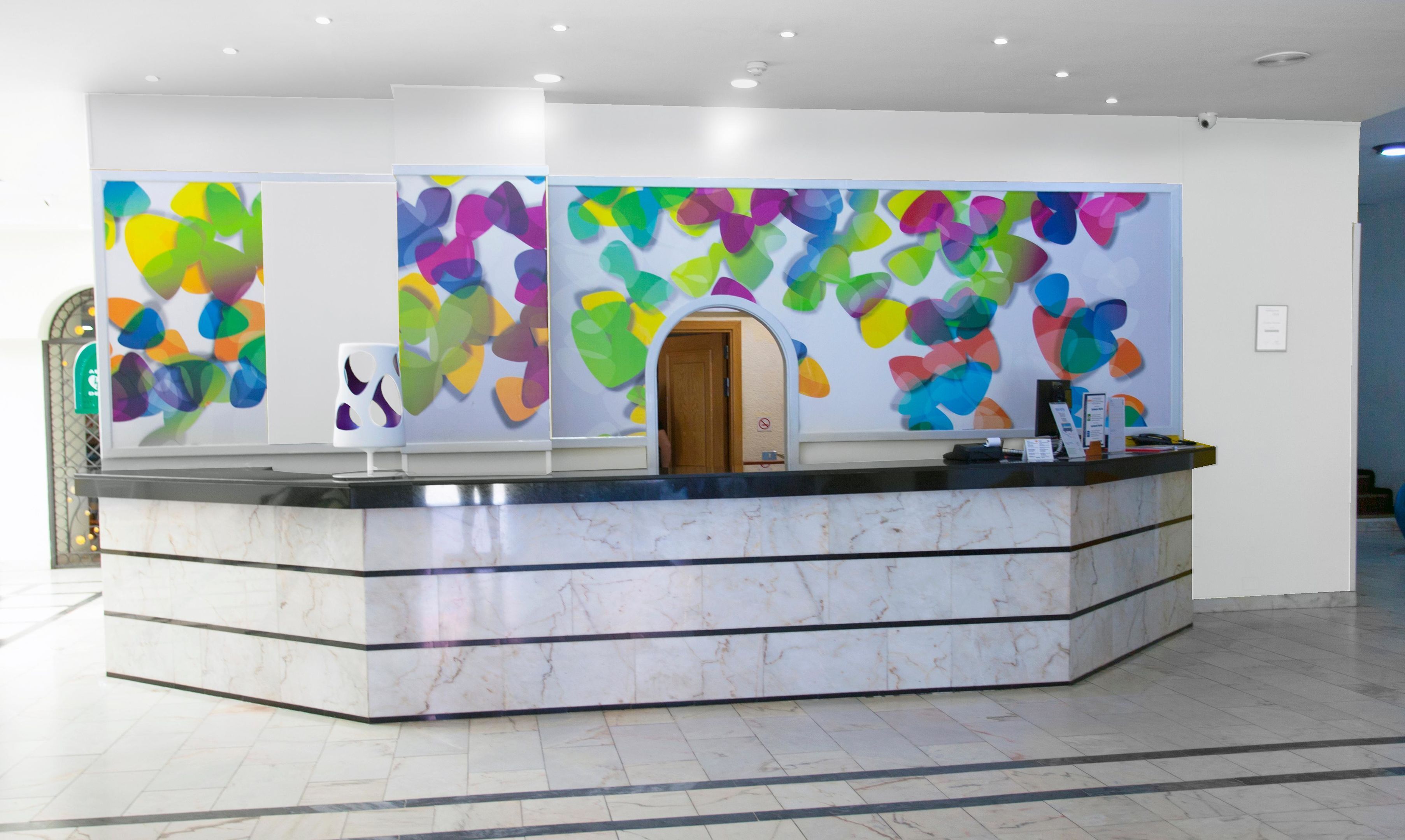 A reception desk with a marble finish, a colorful abstract wall art, and a no-smoking sign.