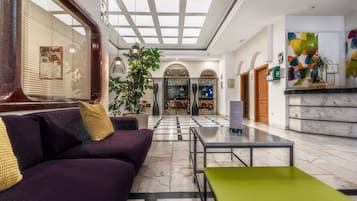 A lobby with a purple sofa, a green table, a large plant, and a reception desk.