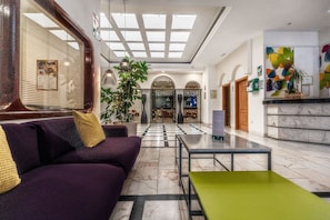 Un hall d’entrée avec un canapé violet, une table verte, une grande plante et un comptoir d’accueil.