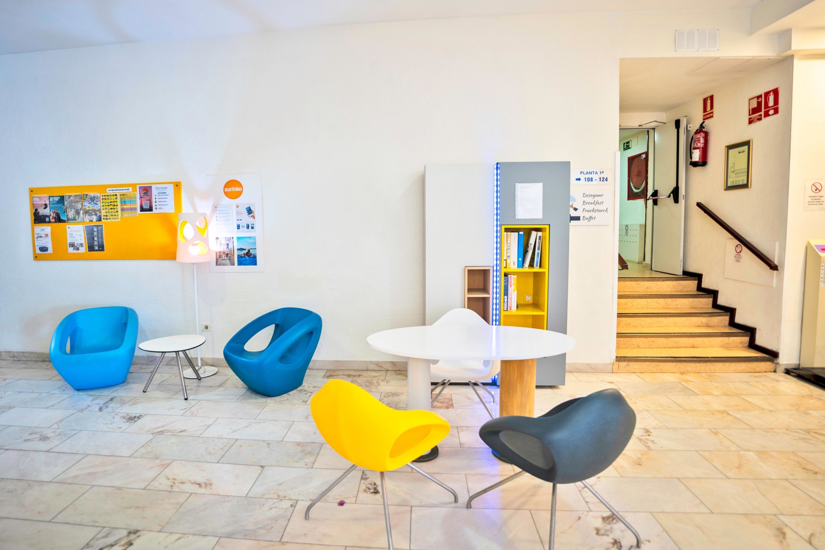 A modern lobby with a bulletin board, a white round table, and colorful chairs.