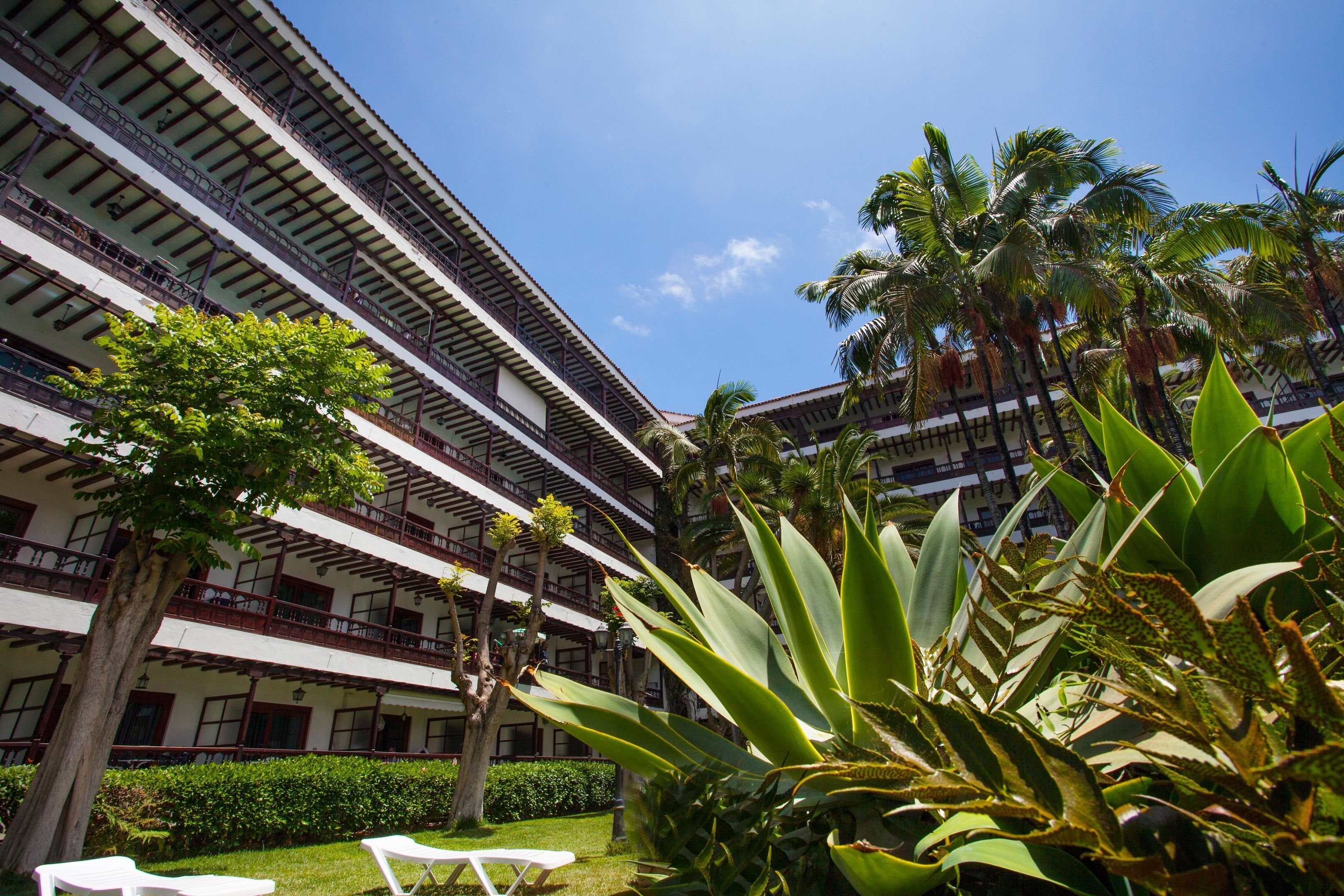 Ein mehrstöckiges Hotel mit Balkonen, üppiger Bepflanzung und blauem Himmel.