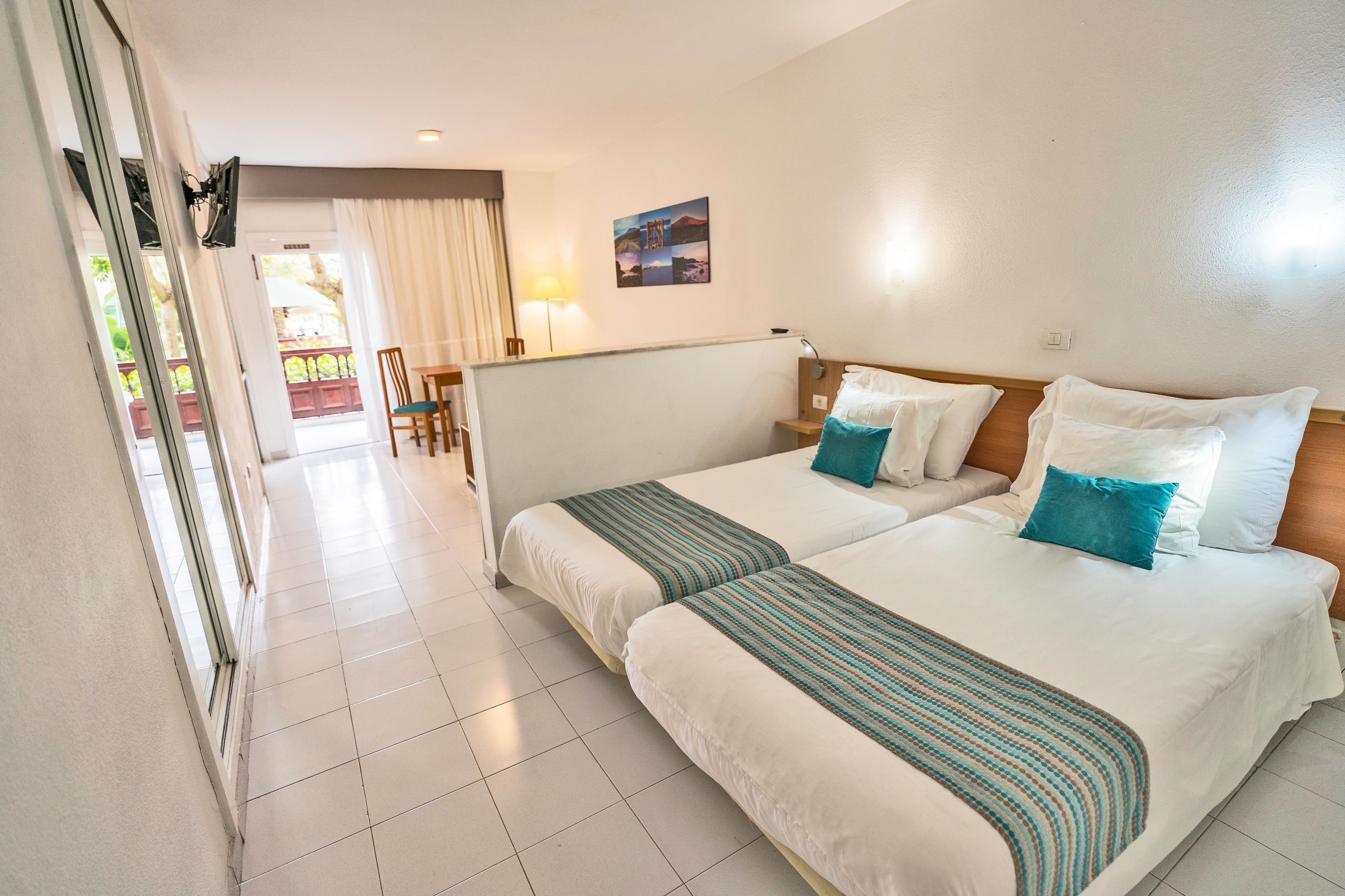 Een hotelkamer met twee bedden, een balkon en uitzicht op de omgeving.