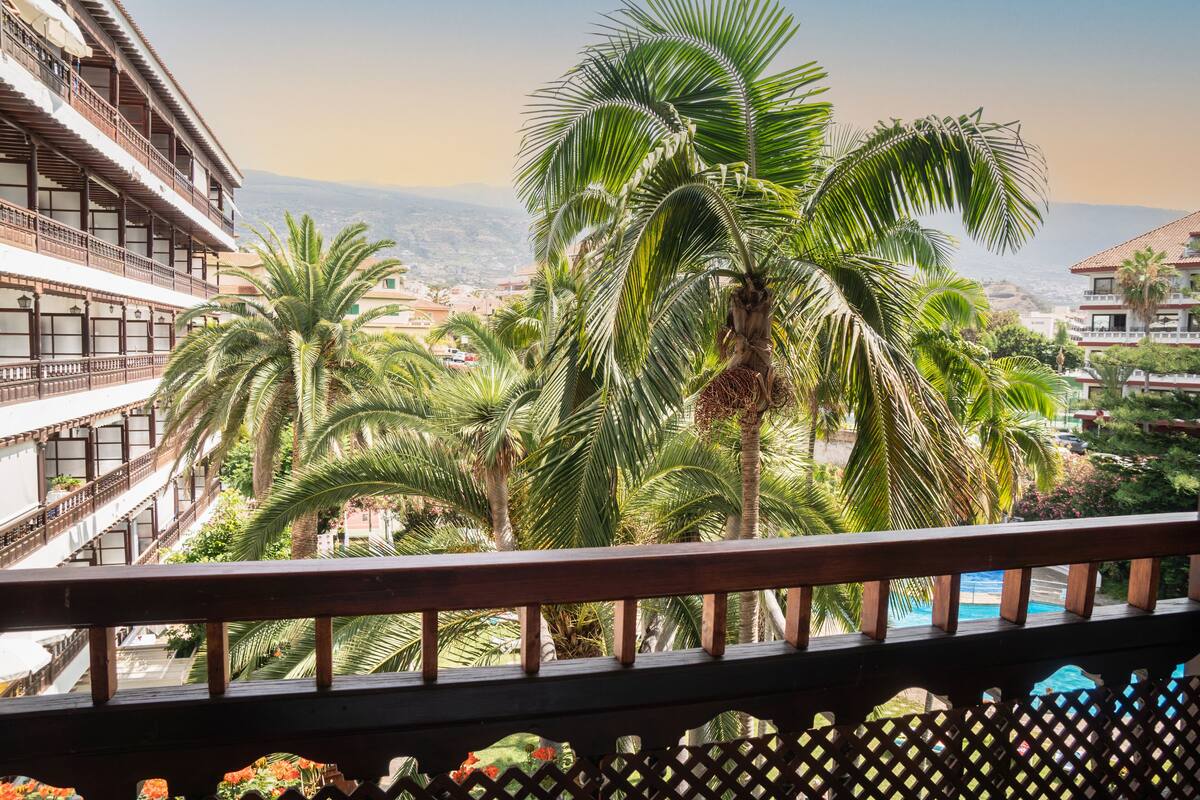 Een balkon met uitzicht op palmbomen en een verre skyline.