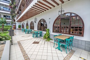 Une terrasse extérieure couverte, dotée d’un sol carrelé, de poutres en bois et de chaises vertes.