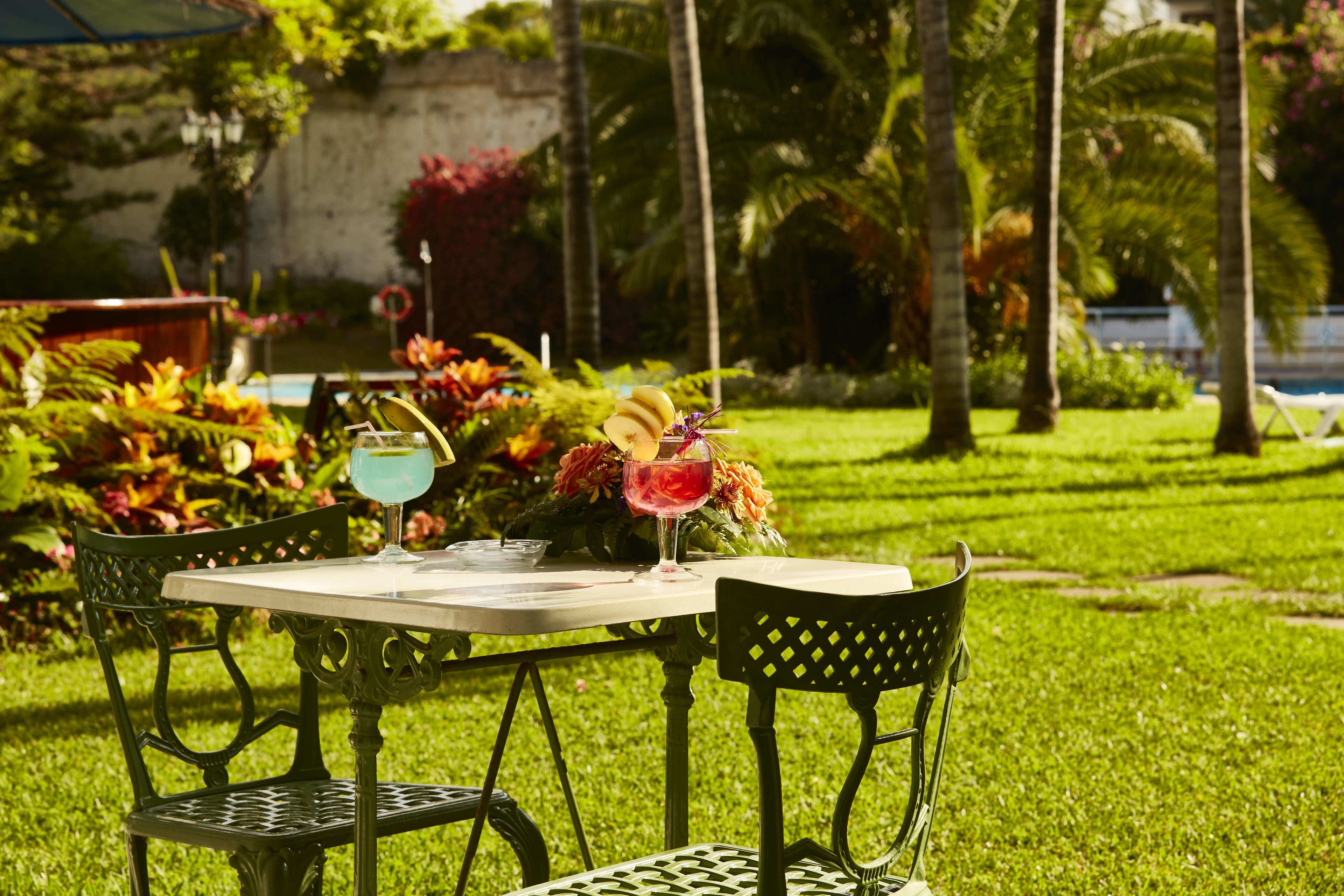 Mesa al aire libre con sillas, una bebida y un arreglo floral.