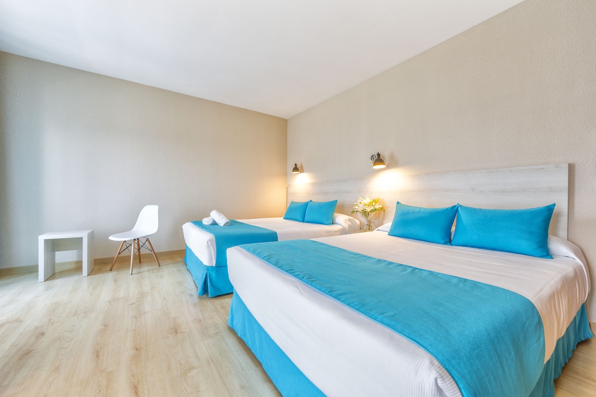 Una habitación de hotel con dos camas, una silla blanca y una mesita.