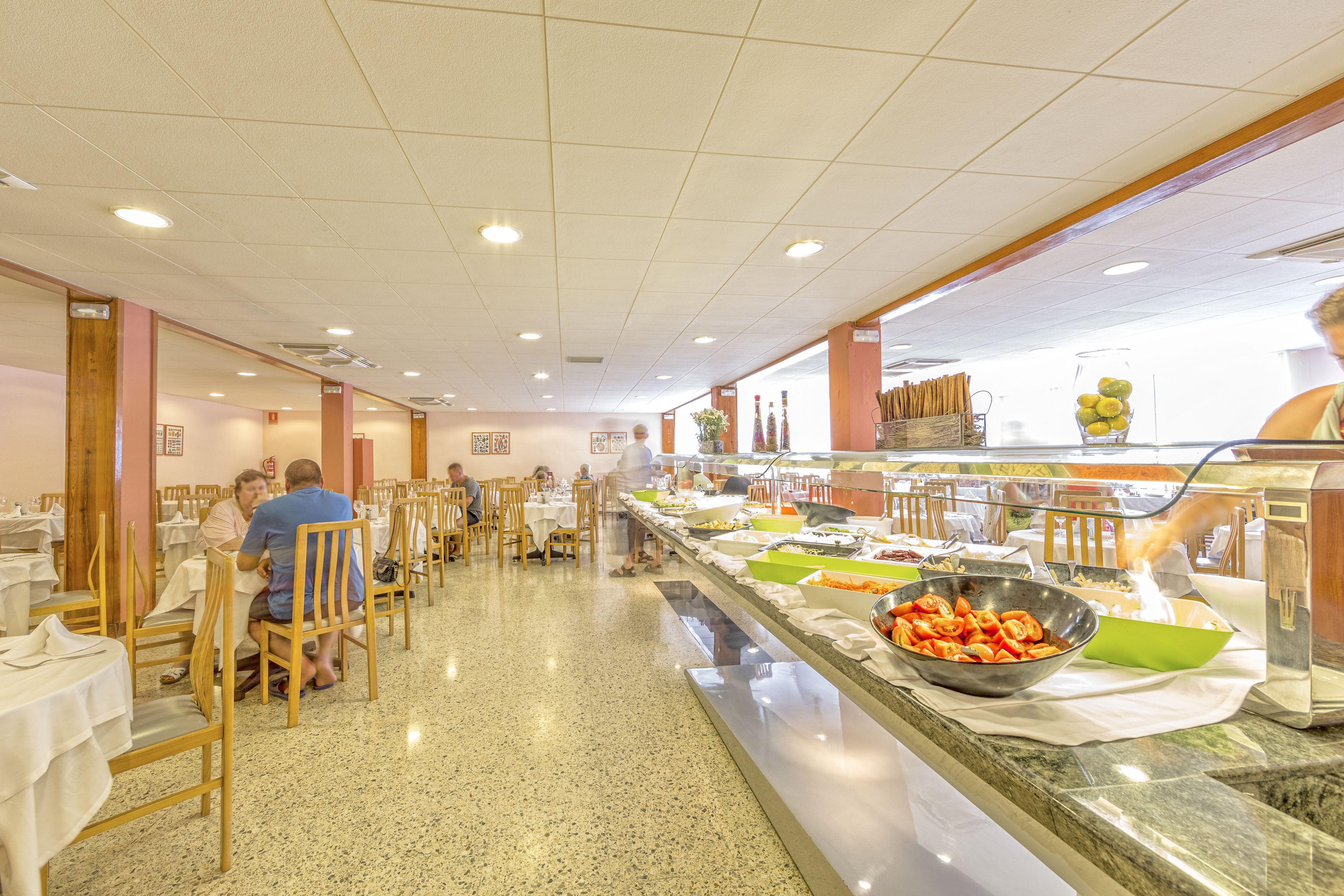 A buffet area with multiple tables and chairs, a variety of food items on display, and a counter with a beverage dispenser.